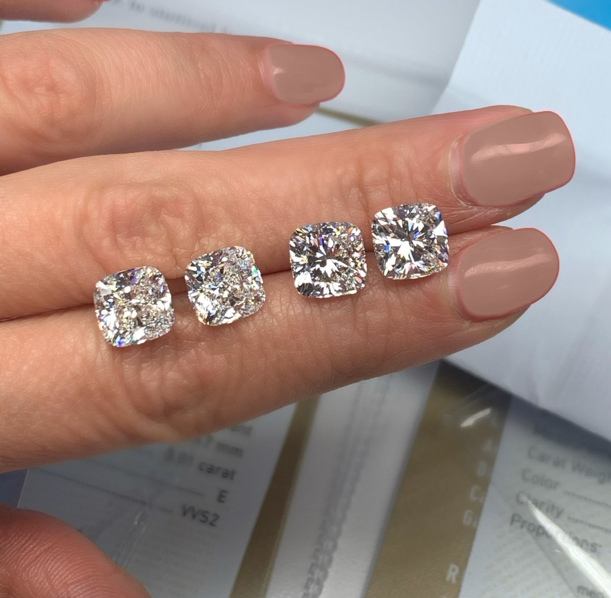 Four loose cushion-cut diamonds balanced on the fingertips above their laboratory grading report