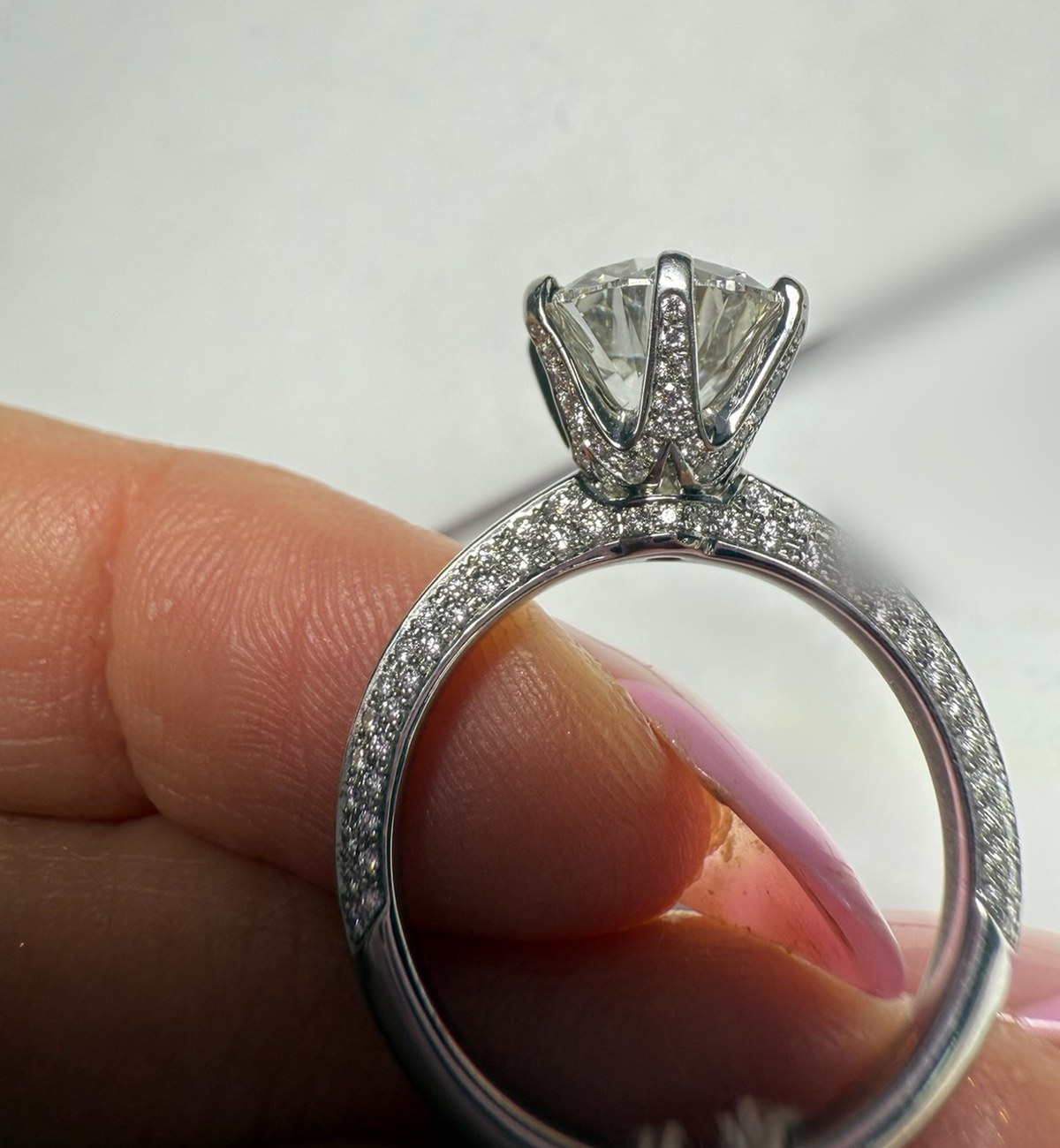 Profile macro of a round diamond solitaire with pavé-set prongs and basket above a three-row pavé shank