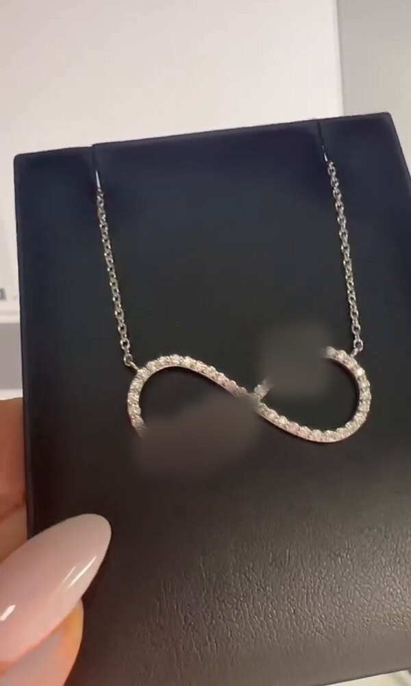 A custom diamond infinity pendant, the personalized lettering and number on its loops deliberately obscured to protect the client who commissioned it