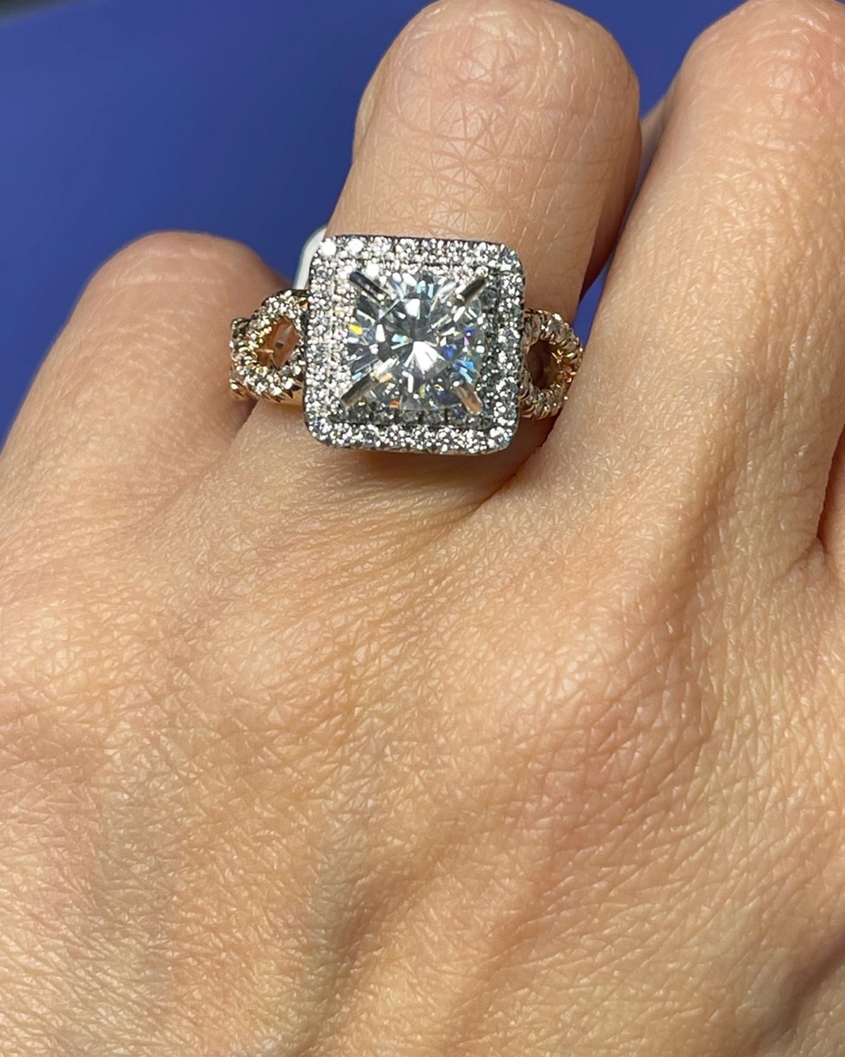 Face-up macro of a princess-cut diamond in a white pavé halo above a rose gold openwork gallery