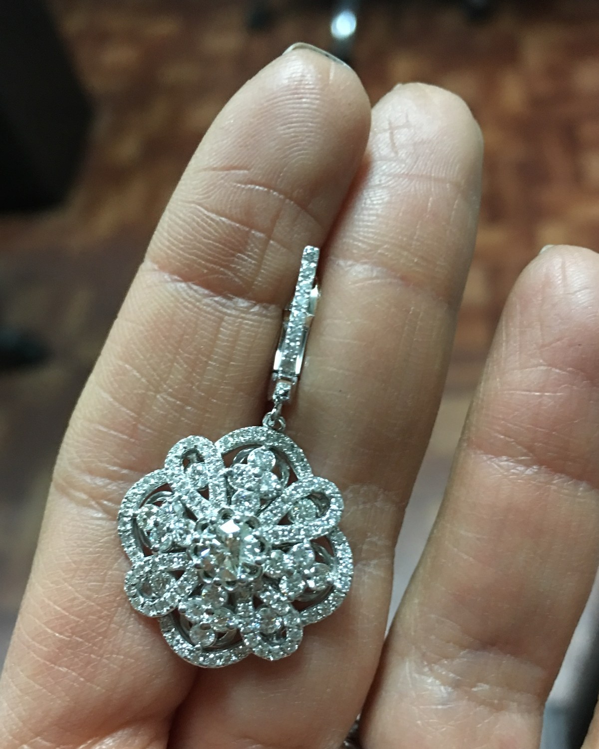 Single white gold floral diamond cluster drop earring held between the fingers, diamond-set link above the cluster