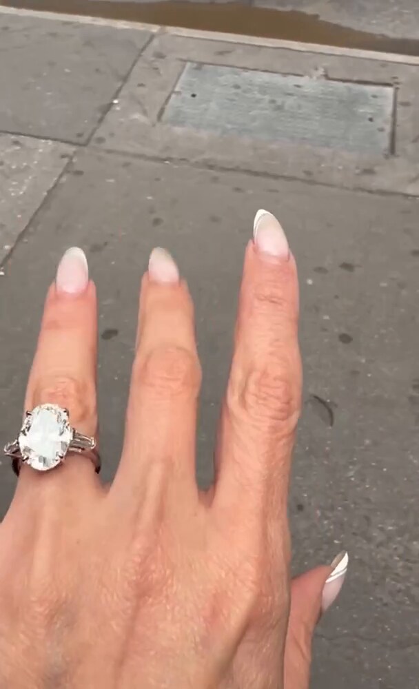 An oval diamond solitaire worn on the hand, moving in daylight on a New York sidewalk